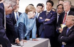 German Chancellor Merkel in an assertive pose planting both hands firmly on a table as she addresses an emotionless US president Trump 