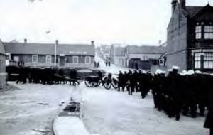 The ship’s company march to Stanley cemetery for the burial of a leading seaman 