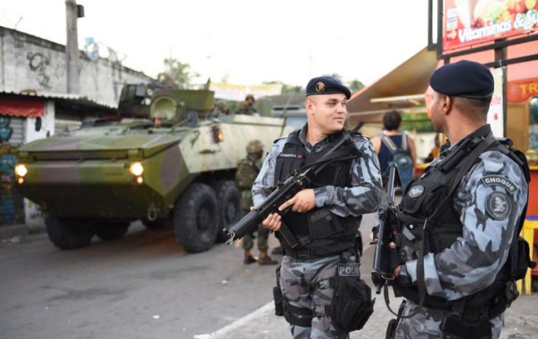 Heavy armed soldiers patrol the streets while people get on with their daily business 