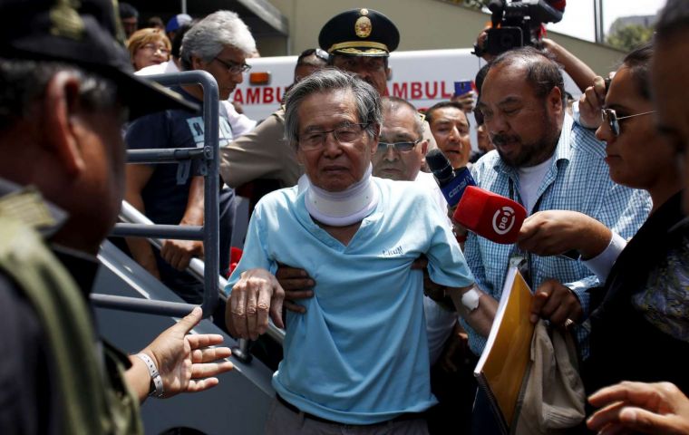 Fujimori lay propped up on a hospital bed wearing a white gown, with a blood pressure cuff on his right arm and another monitor clasped to his left index finger. 