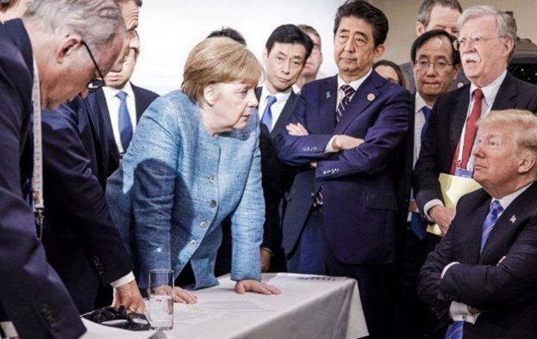 German Chancellor Merkel in an assertive pose planting both hands firmly on a table as she addresses an emotionless US president Trump 