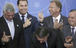 Beaming members of Congress and industry lobbyists clapped and made pistol signs with their hands as Bolsonaro relaxed rules on weapons 