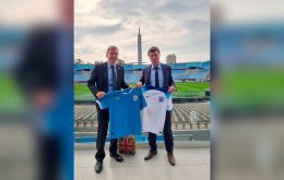Minister Rutley with a Uruguayan team shirt and a local football authority holds a Lionesses color